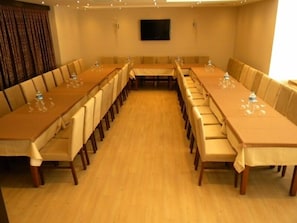 Una sala conferenze con lunghe tavolate, sedie e una televisione a schermo piatto appesa al muro.