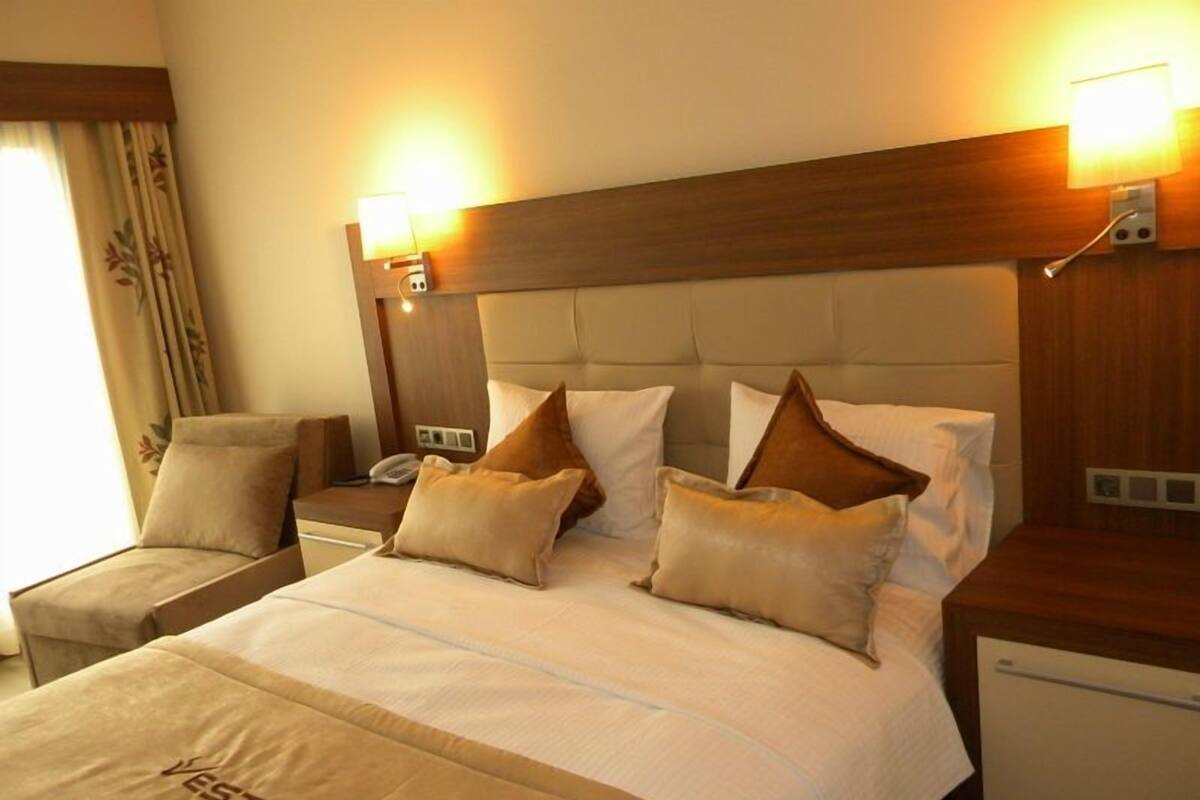 A hotel room with a large bed, two bedside tables, a nightstand, a lamp, and a small bedside table with a phone.