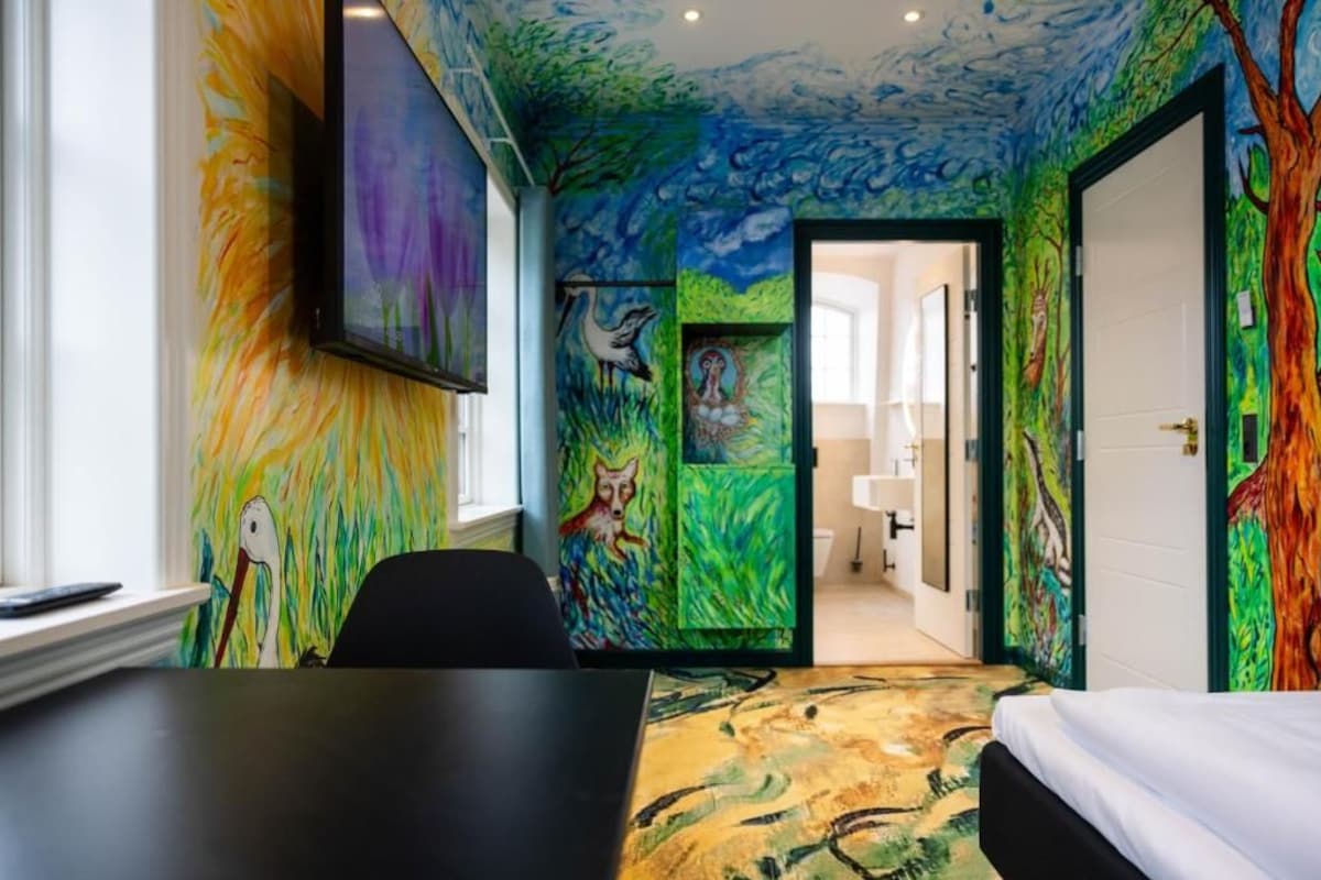 A room with vibrant wall art, a bed, a desk, and a TV.