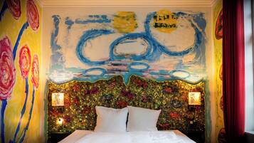 A room with a bed, a colorful abstract mural on the wall, and two wall-mounted lamps.