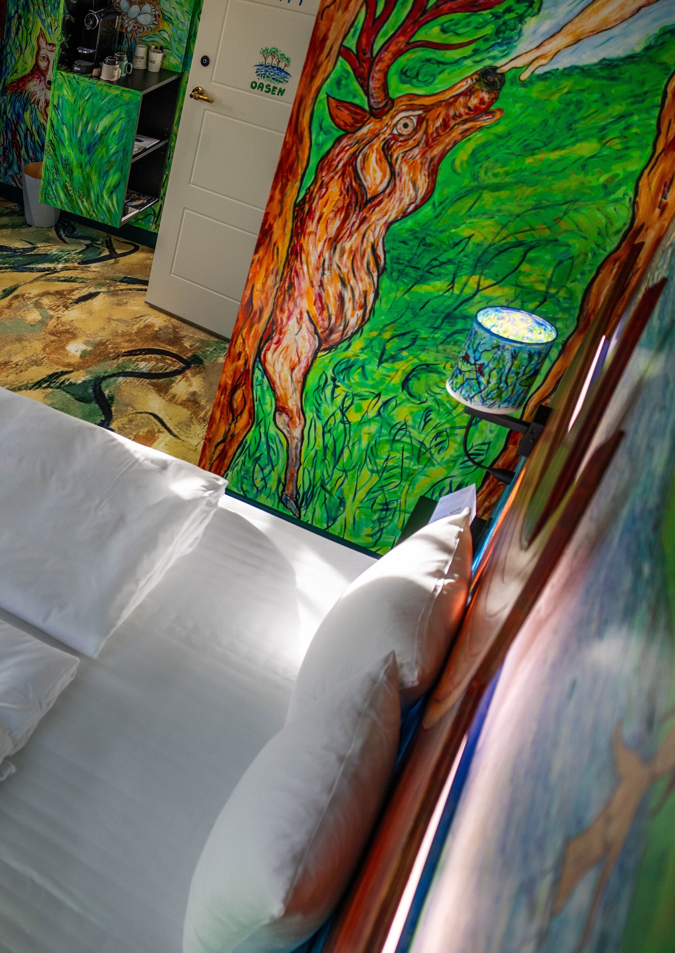 A bed with a colorful painting of a deer and a tree, a white door, and a small cabinet with a logo.