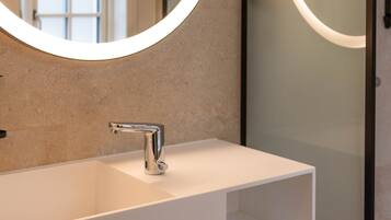 A bathroom with a white sink, a round mirror with a light, and a frosted glass door.