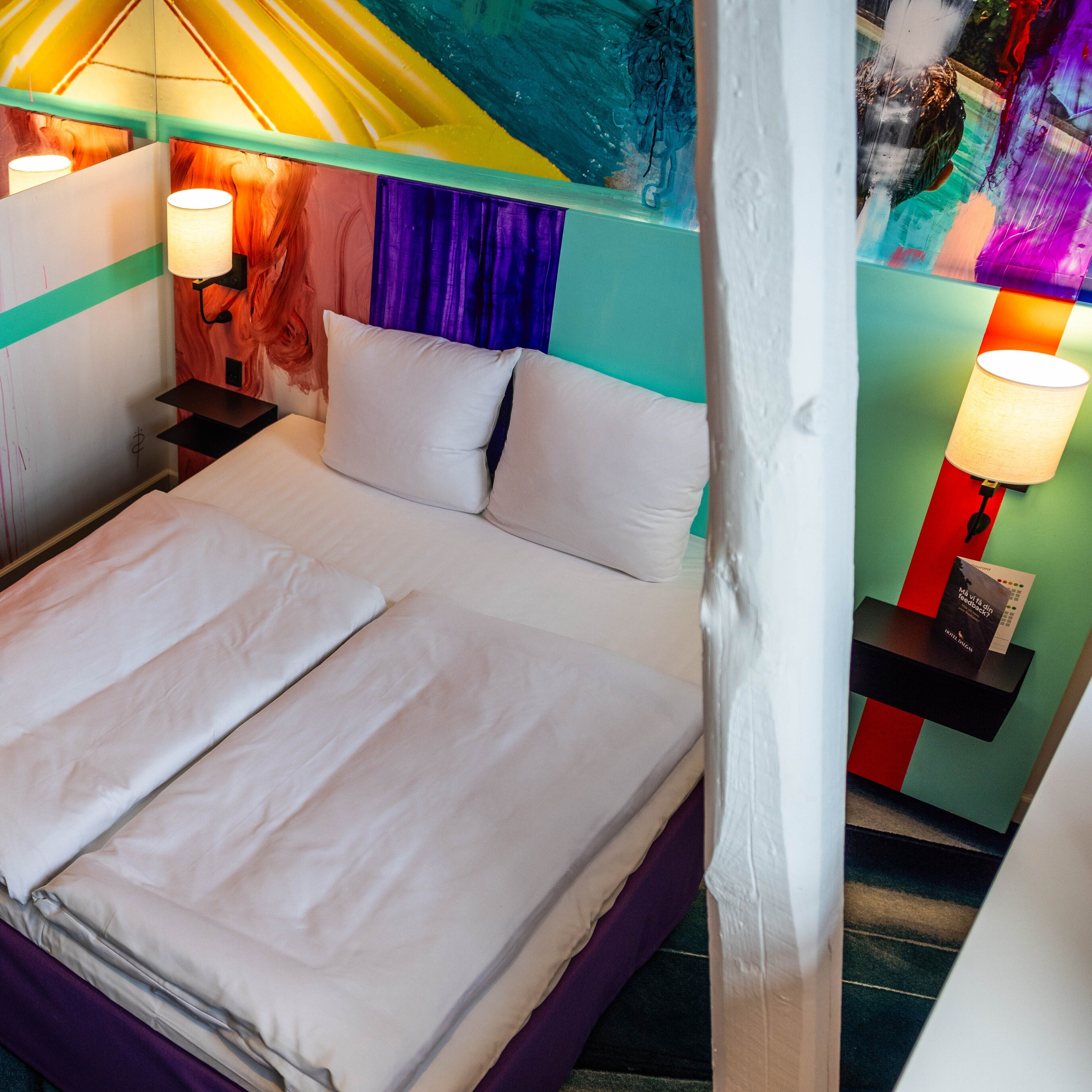 A bed with white linens in a room with colorful walls and a mural.