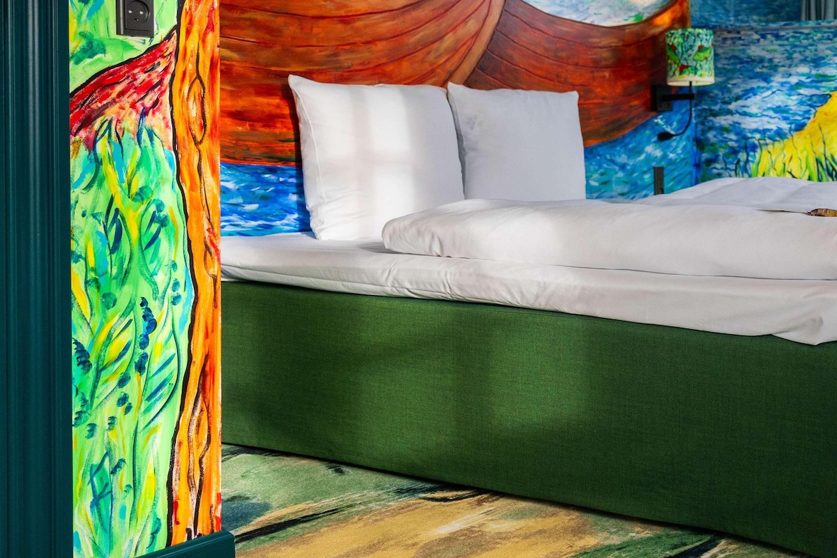 A bedroom with a bed, a mural on the wall, and a window.