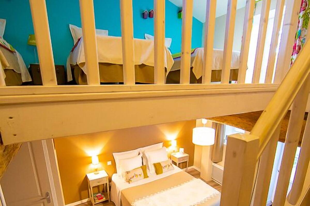Une chambre à coucher avec un escalier en bois, un lit recouvert de draps blancs, une table de chevet et une lampe fixée au mur.