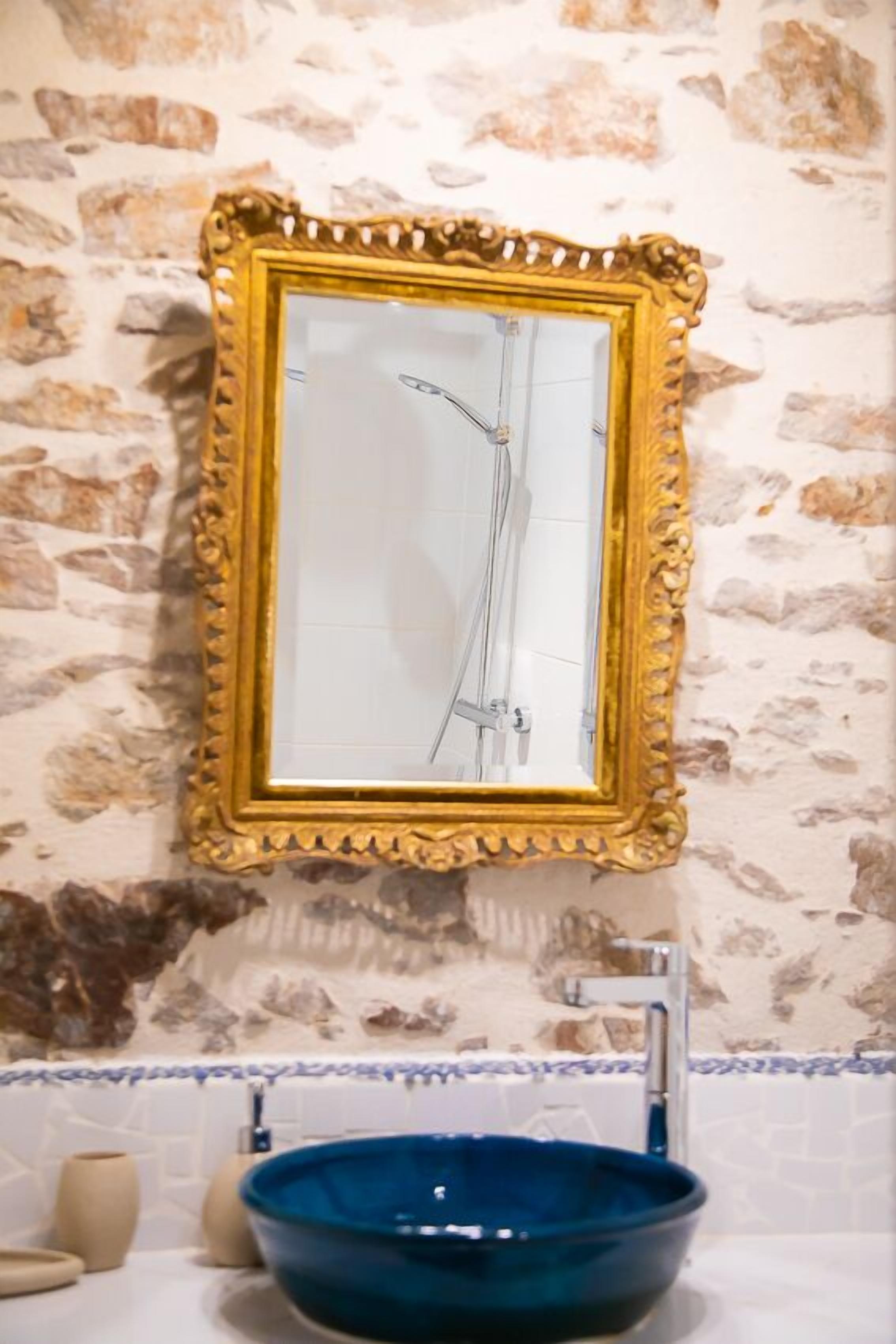 A bathroom with a stone wall, a gold-framed mirror, and a blue sink.