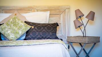 A neatly made bed with patterned pillows, a bedside lamp, and a wicker side table.