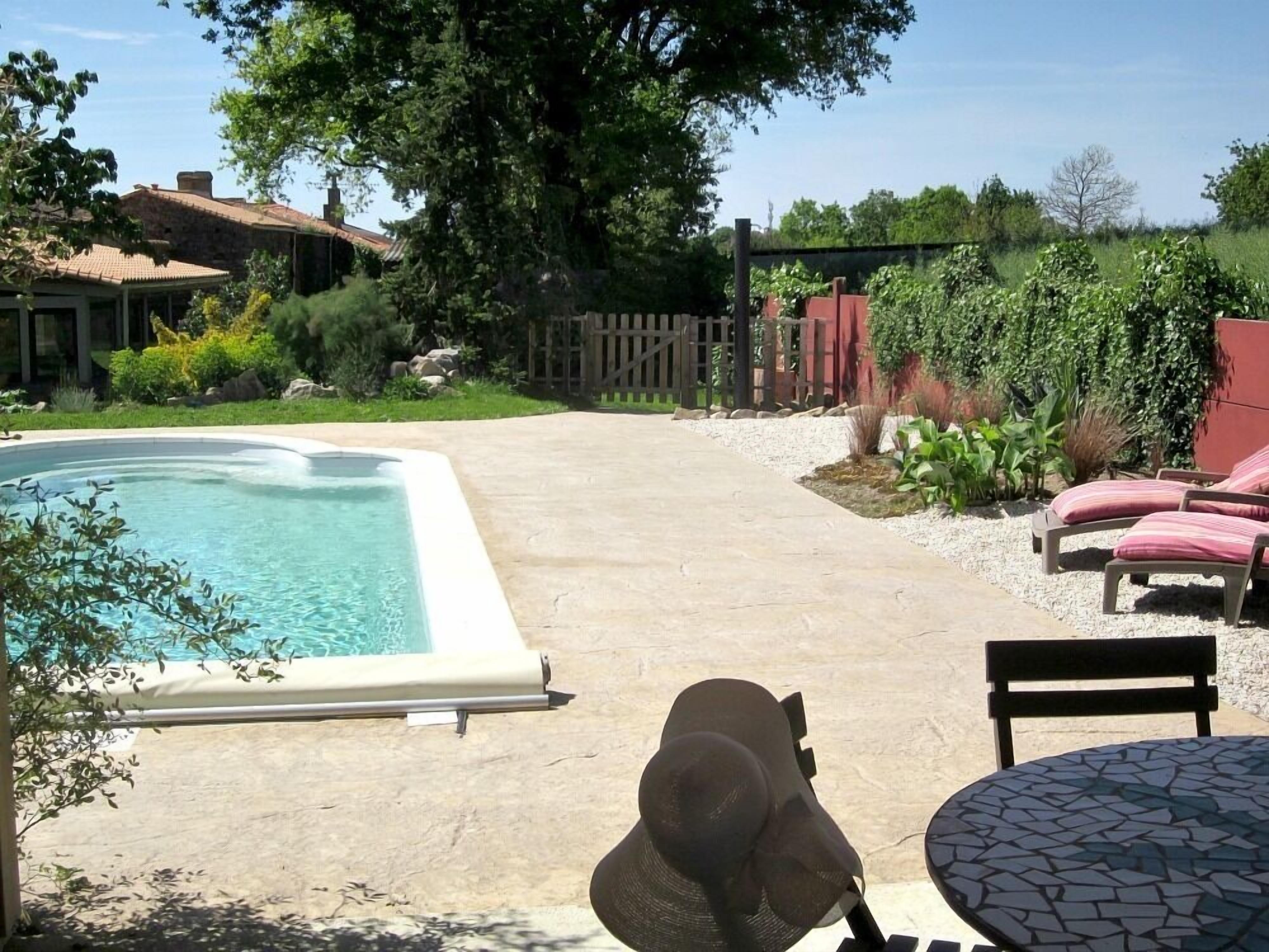 Ein Garten mit Swimmingpool, Terrassentisch und Liegestühlen.