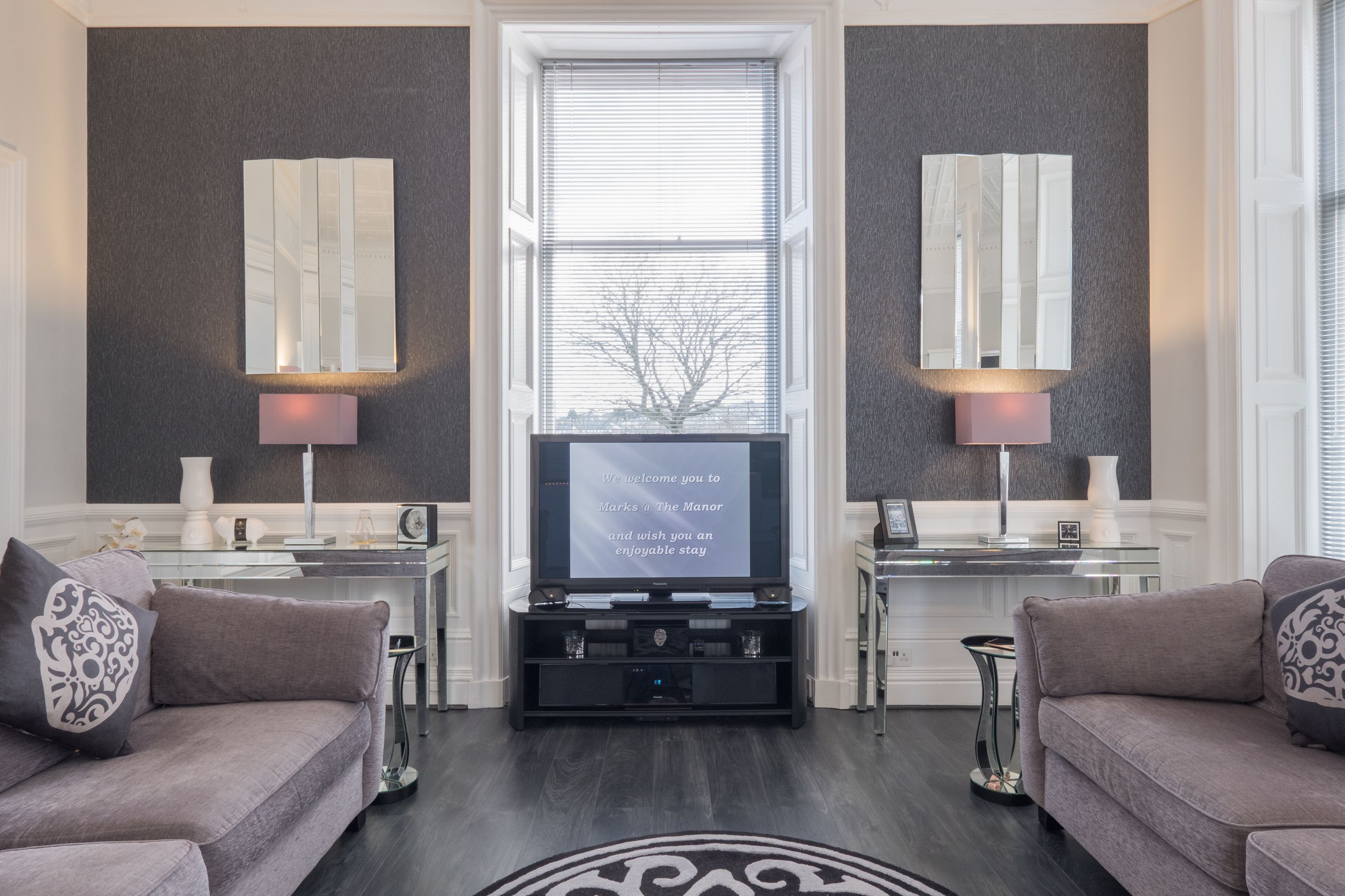 Una sala de estar moderna con un televisor de pantalla plana grande, dos sofás, una mesa de centro de vidrio y lámparas decorativas.