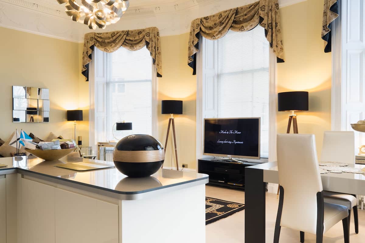 A modern living room with a large TV, a dining table, and a kitchen area with a bowl on the counter.
