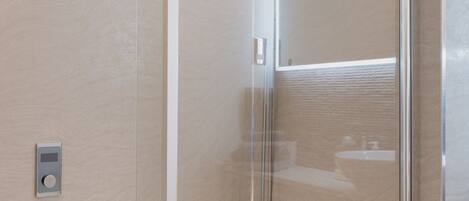 A modern bathroom with a glass-enclosed shower, a white bathtub, and a visible control panel.
