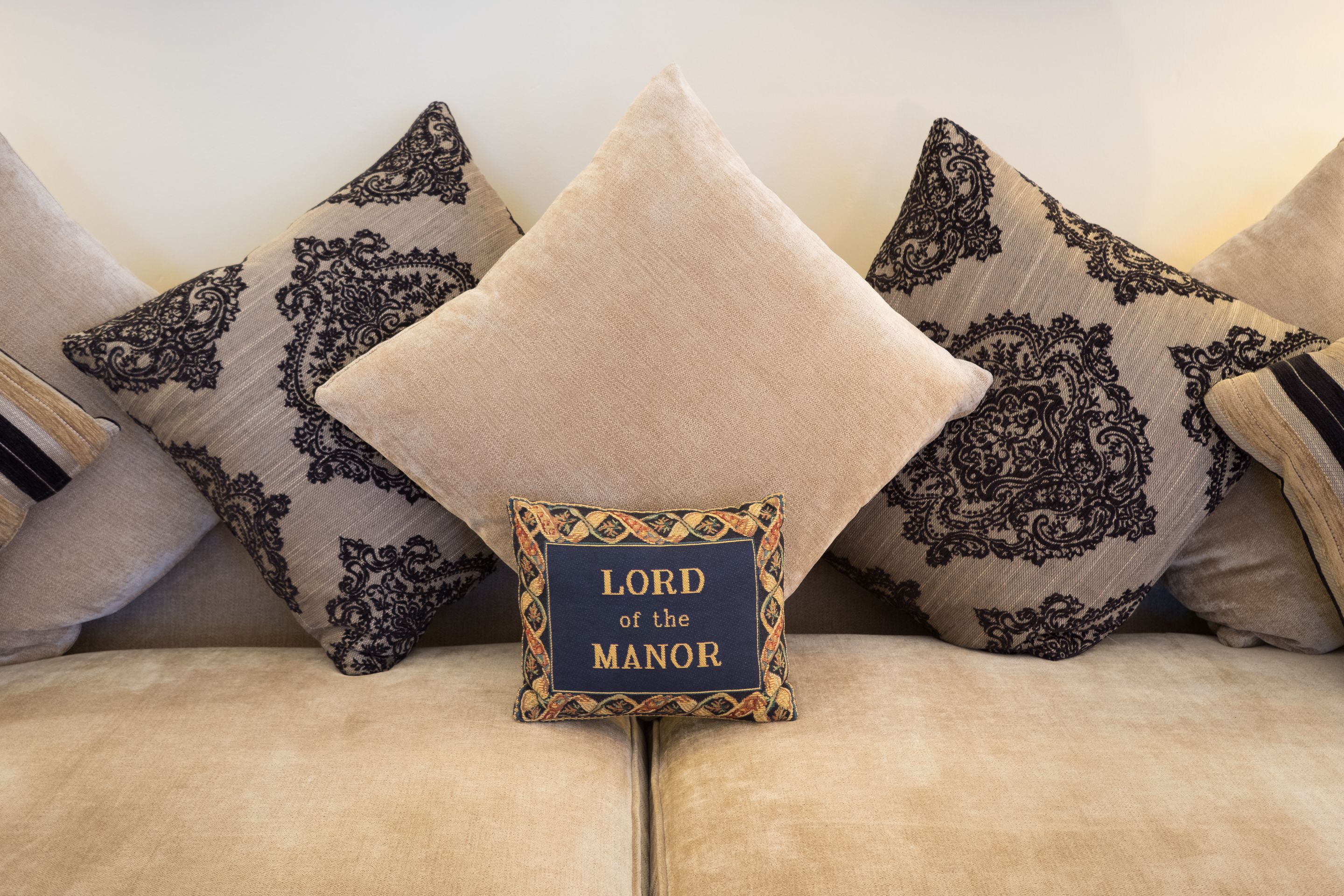 A sofa with decorative pillows, one with a label reading "LORD of the Manor".