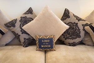 Een bank met decoratieve kussens, waarvan er één de tekst 'LORD of the Manor' bevat.