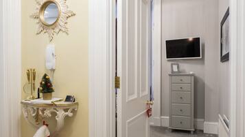 A narrow hallway with a white door, a small Christmas tree, a mirror, a telephone, and a television on a dresser.