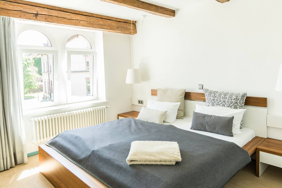 A bedroom with a large bed, wooden headboard, and a window with curtains.