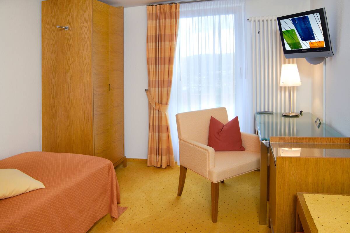 A hotel room with two beds, a chair, a desk, a TV, and a lamp.