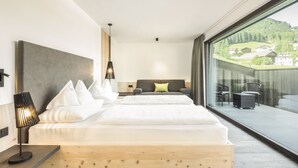A modern hotel room with a large bed, a small sofa, a table, and a balcony with a view of the countryside. - Garni Hotel Pra Palmer (Castelrotto)
