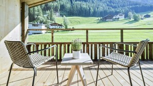 A wooden deck with two wicker chairs and a table, overlooking a green landscape with houses and trees. - Garni Hotel Pra Palmer (Castelrotto)