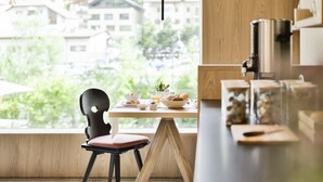 A dining area with a table set for breakfast, a chair, and a view of buildings and greenery outside. - Garni Hotel Pra Palmer (Castelrotto)