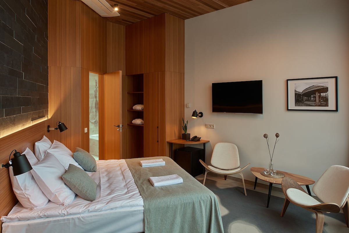 Een moderne hotelkamer met een bed, twee stoelen, een tafeltje, een televisie en een ingelijst kunstwerk aan de muur.