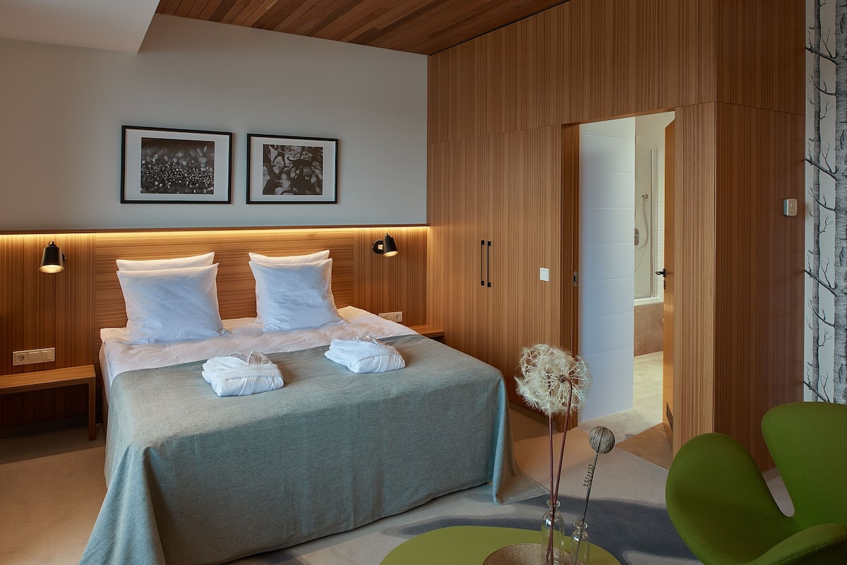Een moderne hotelkamer met een groot bed, een houten hoofdbord, twee ingelijste foto’s aan de muur en een groene stoel.