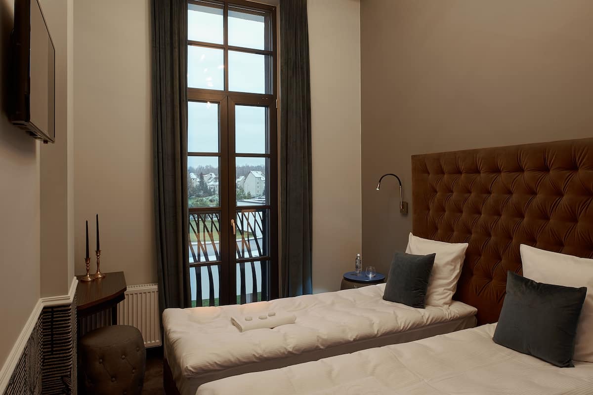 Een hotelkamer met twee bedden, een groot raam, een radiator, een klein tafeltje en een tv aan de muur.