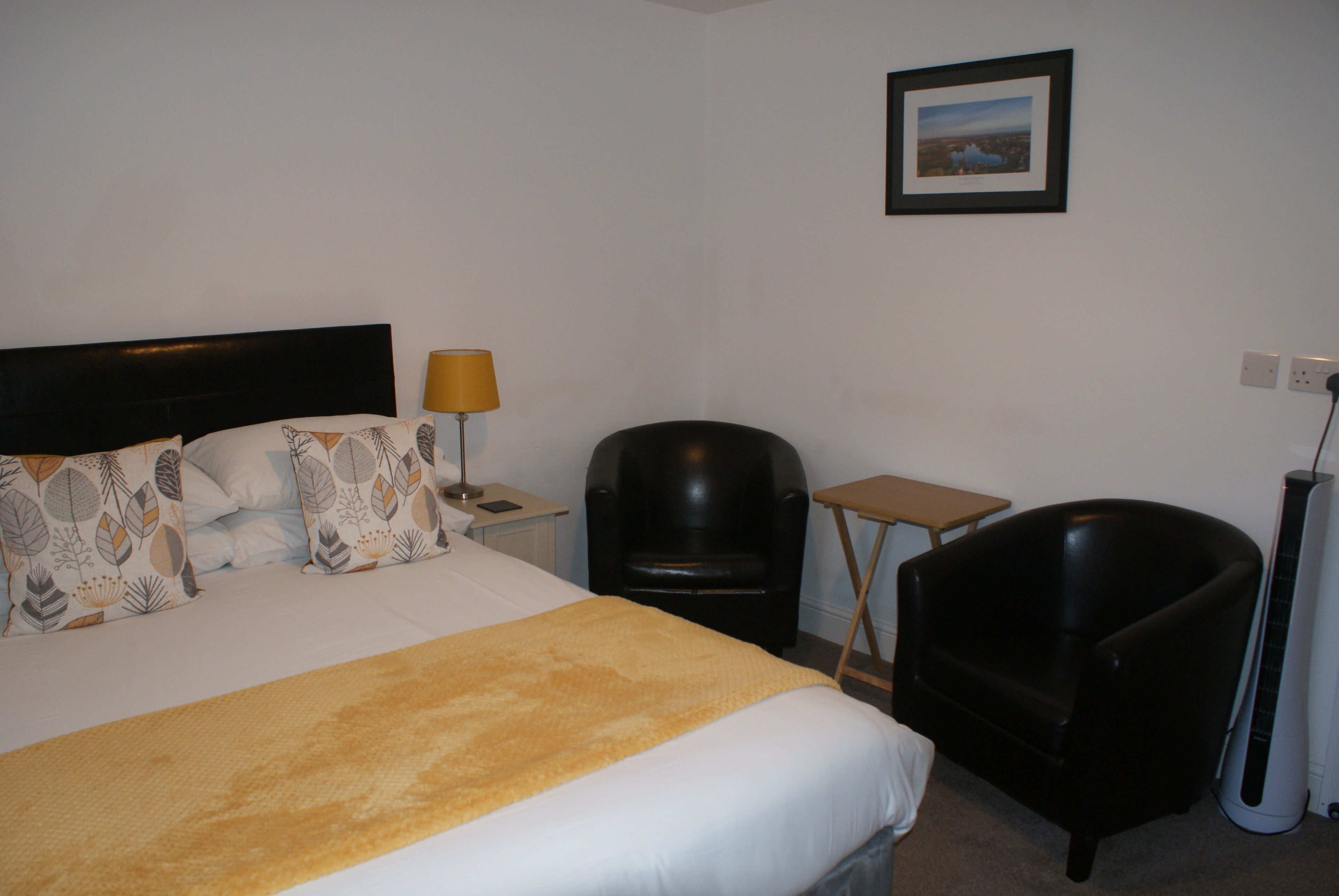 A hotel room with a bed, two chairs, a small table, a lamp, and a picture on the wall.