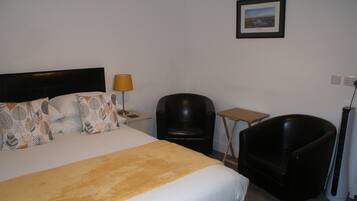 A hotel room with a bed, two chairs, a small table, a lamp, and a picture on the wall.