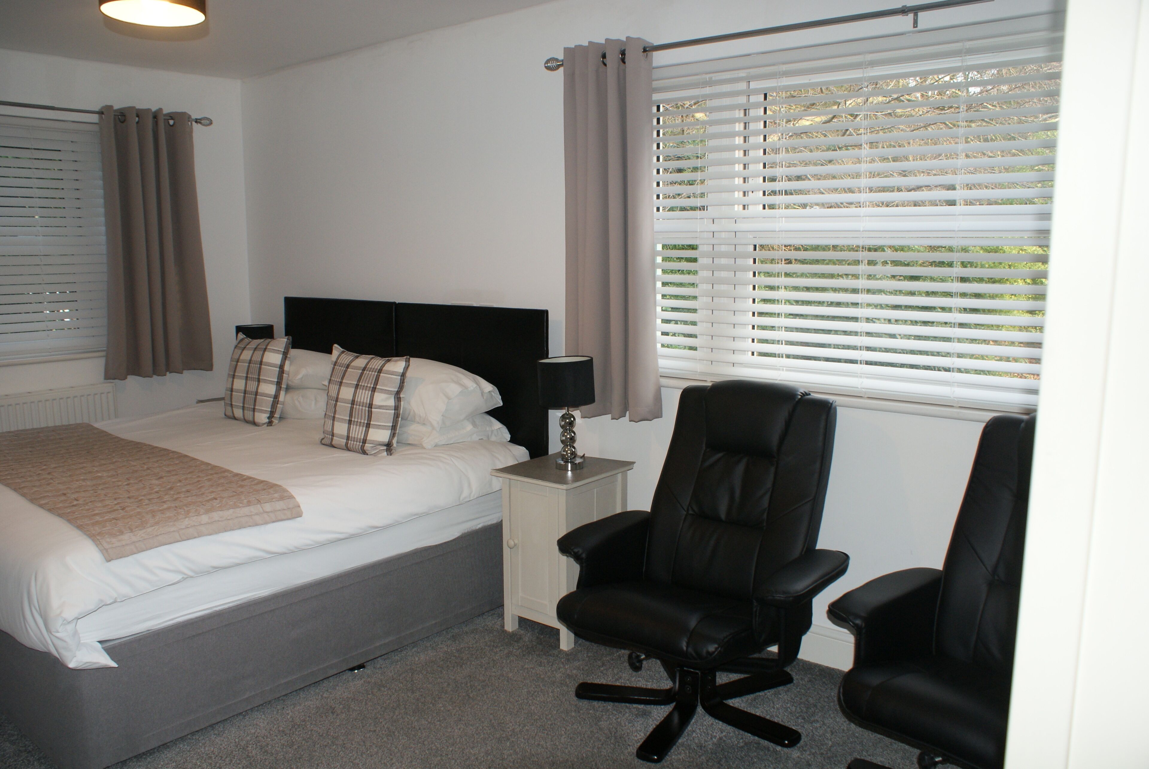 A bedroom with a bed, two chairs, a nightstand, and a window with blinds.