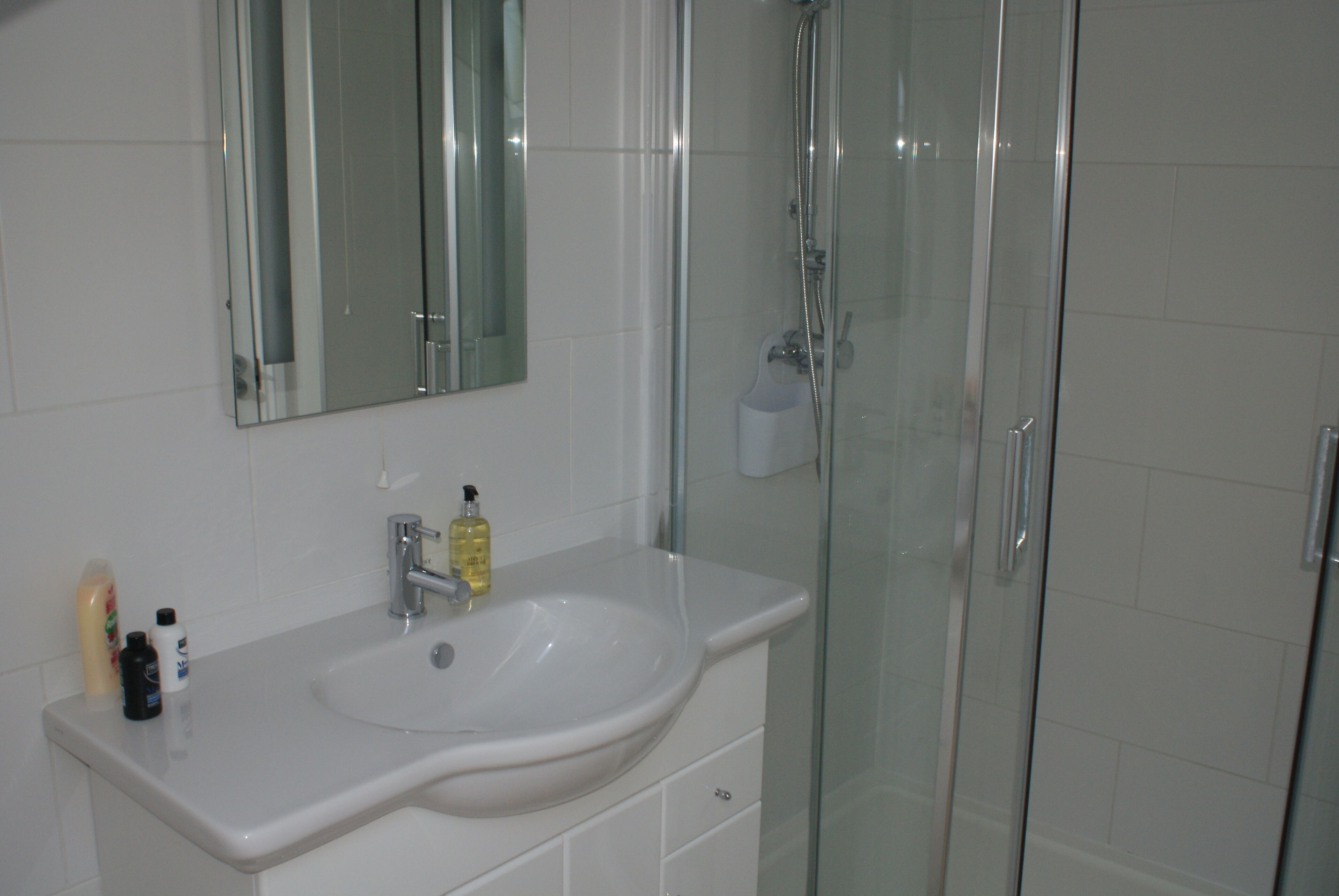 Un baño con lavamanos blanco, espejo y cabina de ducha de vidrio.