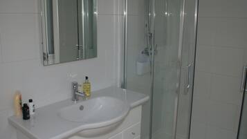 Un baño con lavamanos blanco, espejo y cabina de ducha de vidrio.