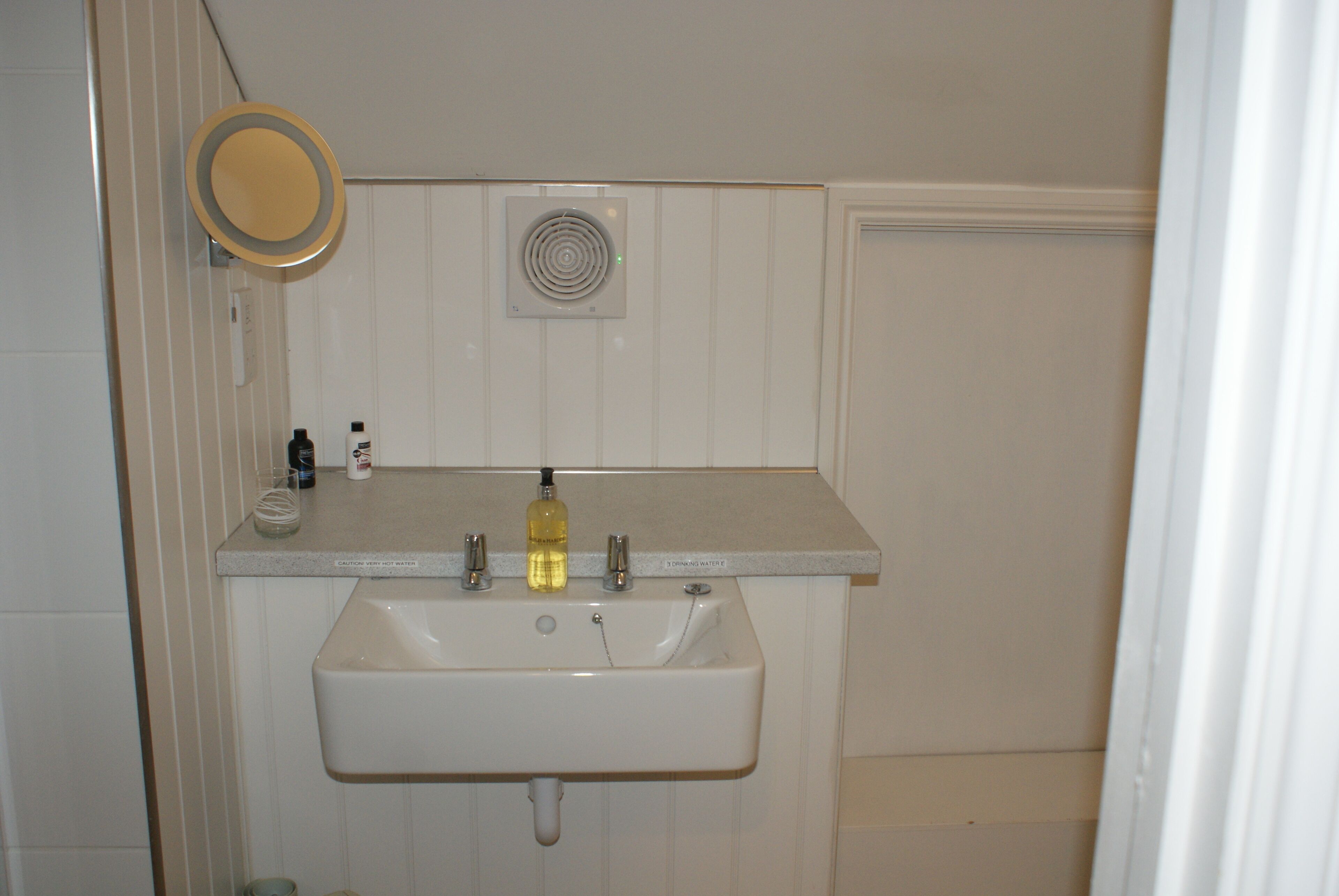 Un baño con un lavamanos blanco, un espejo y un ventilador.