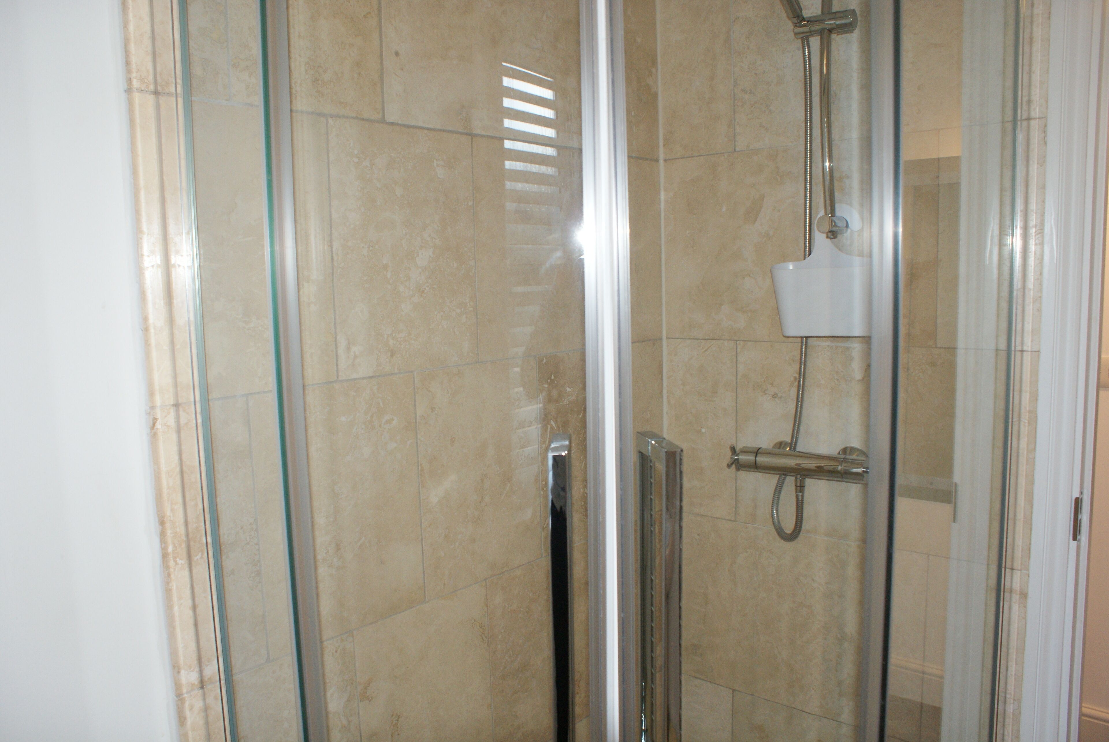 Un área de ducha con paredes de vidrio, con cabezal de ducha de mano y llave de pared.