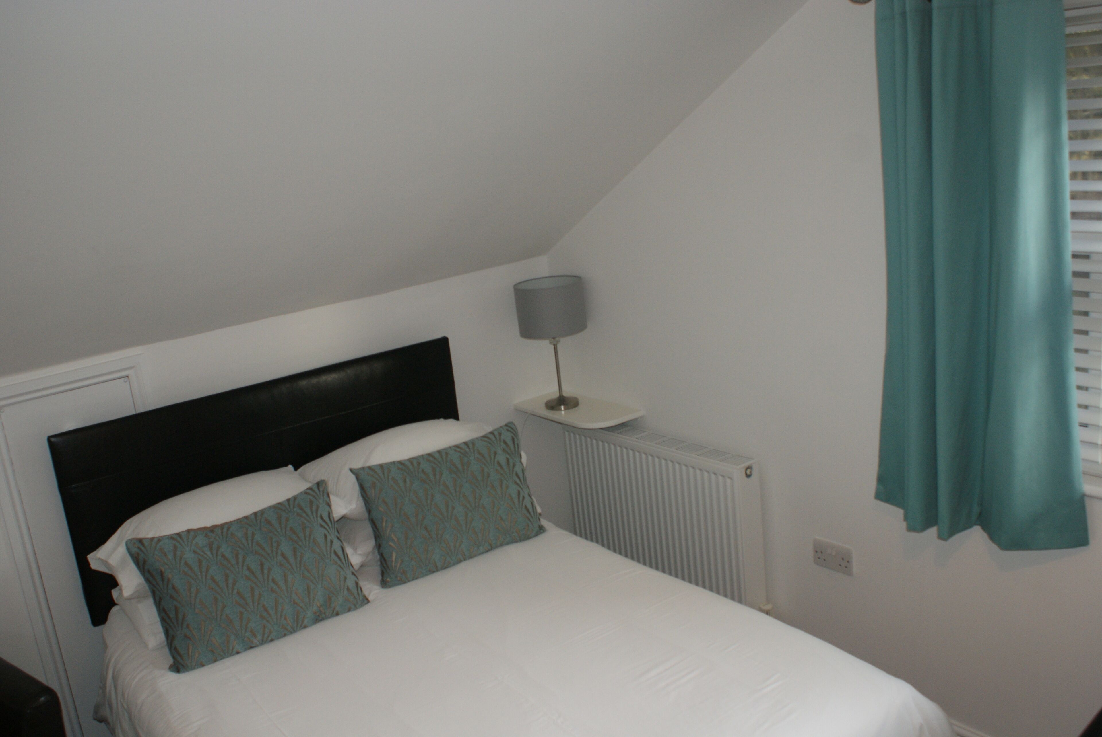 A bedroom with a bed, a nightstand, a lamp, and a window with curtains.