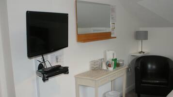 A hotel room with a TV, a mirror, a desk with a lamp, and a chair.