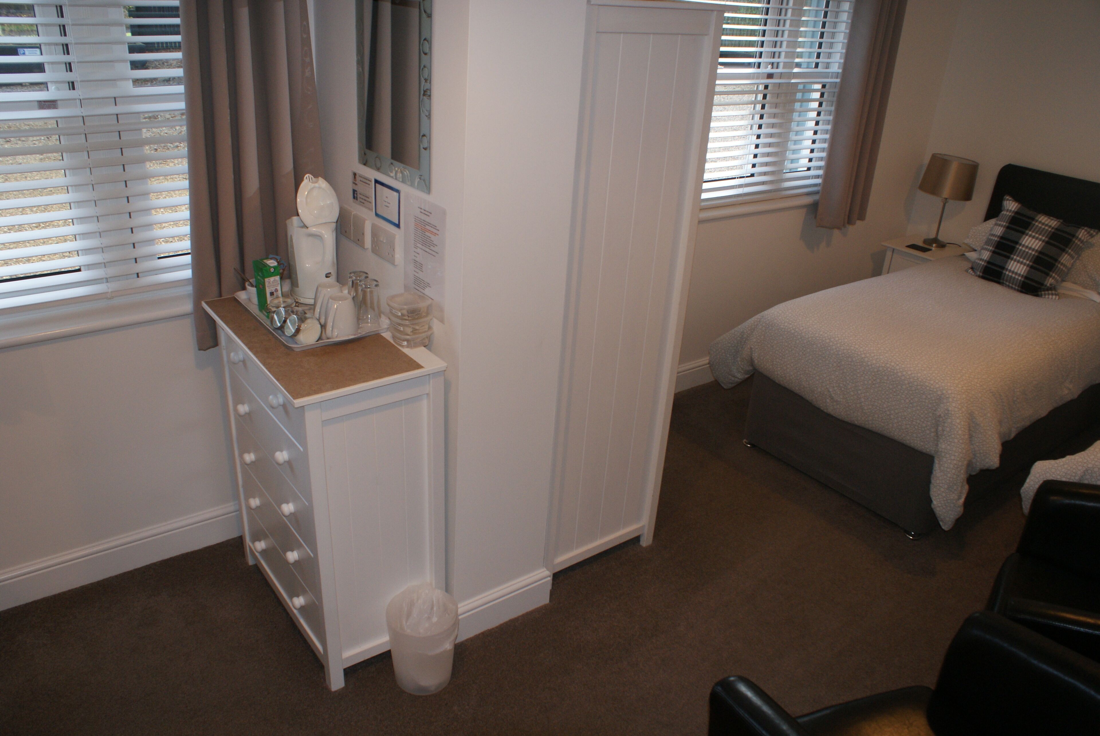 A bedroom with a bed, a dresser, a mirror, and a window with blinds.