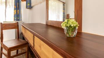A wooden dining table with a vase of flowers, a wooden chair, and a window with curtains.