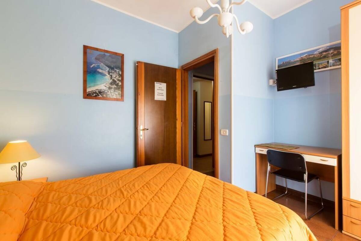 Ein Zimmer mit einem Bett, einem Schreibtisch, einem Stuhl, einem Fernseher und einer Tür.