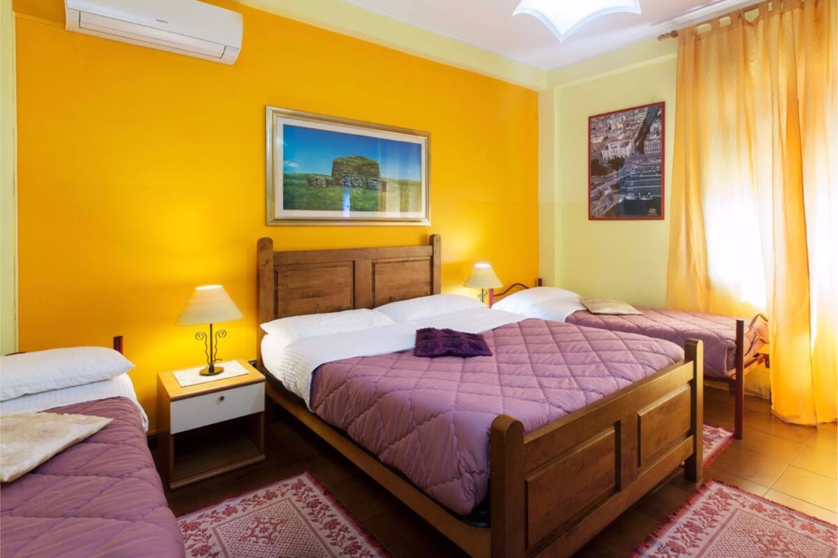Ein Hotelzimmer mit einem hölzernen Bett, zwei Nachttischen, einer Lampe, einem Bilderrahmen und einem Fenster mit Vorhängen.