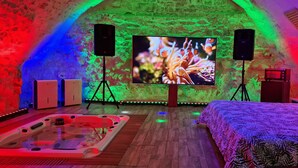 A room with a large TV, two speakers, a hot tub, and a bed with a patterned bedspread. - Chez Stephanie (Chateauroux)