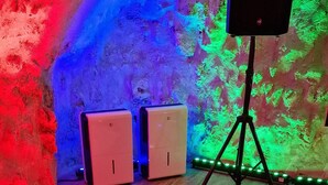 A hot tub with a wooden floor, a speaker on a tripod, and a wall with colorful lighting. - Chez Stephanie (Chateauroux)