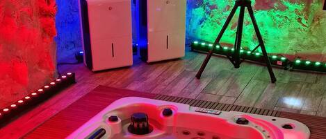 Un jacuzzi con piso de madera, un altavoz sobre un trípode y una pared con iluminación de colores.