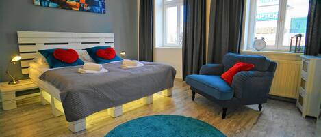 A modern bedroom with a bed, a chair, a blue rug, and a window with curtains.