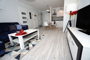 En moderne stue med en blå sofa, et hvidt sofabord og et fjernsyn på et hvidt skab.