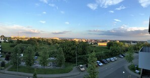 A parking lot with several cars, a grassy area with trees, and a view of a distant cityscape. - City Panorama Apartment (Szczecin)