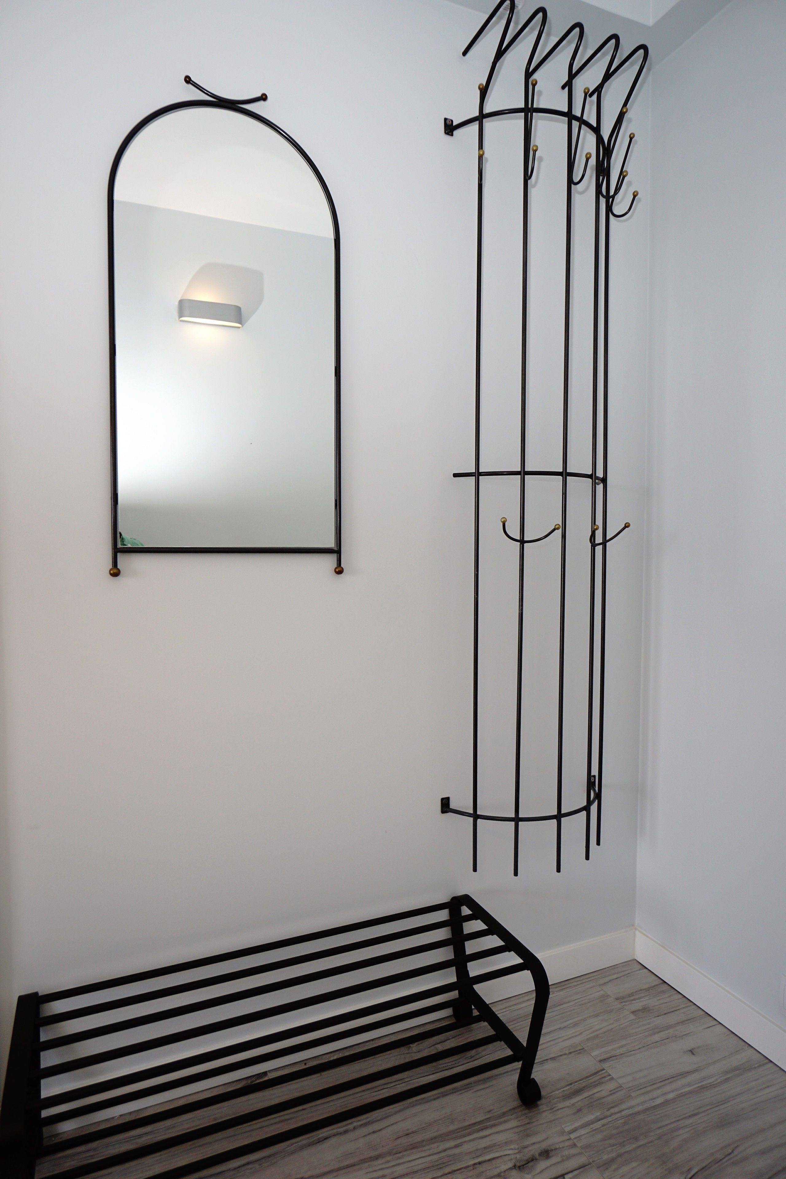 A room with a black metal bench, a wall-mounted mirror, and a vertical metal rack with hooks.