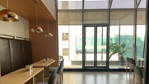 A modern restaurant with a high ceiling, large windows, and a view of a construction site. - ibis Styles Kunming Nanping Hotel (Kunming)