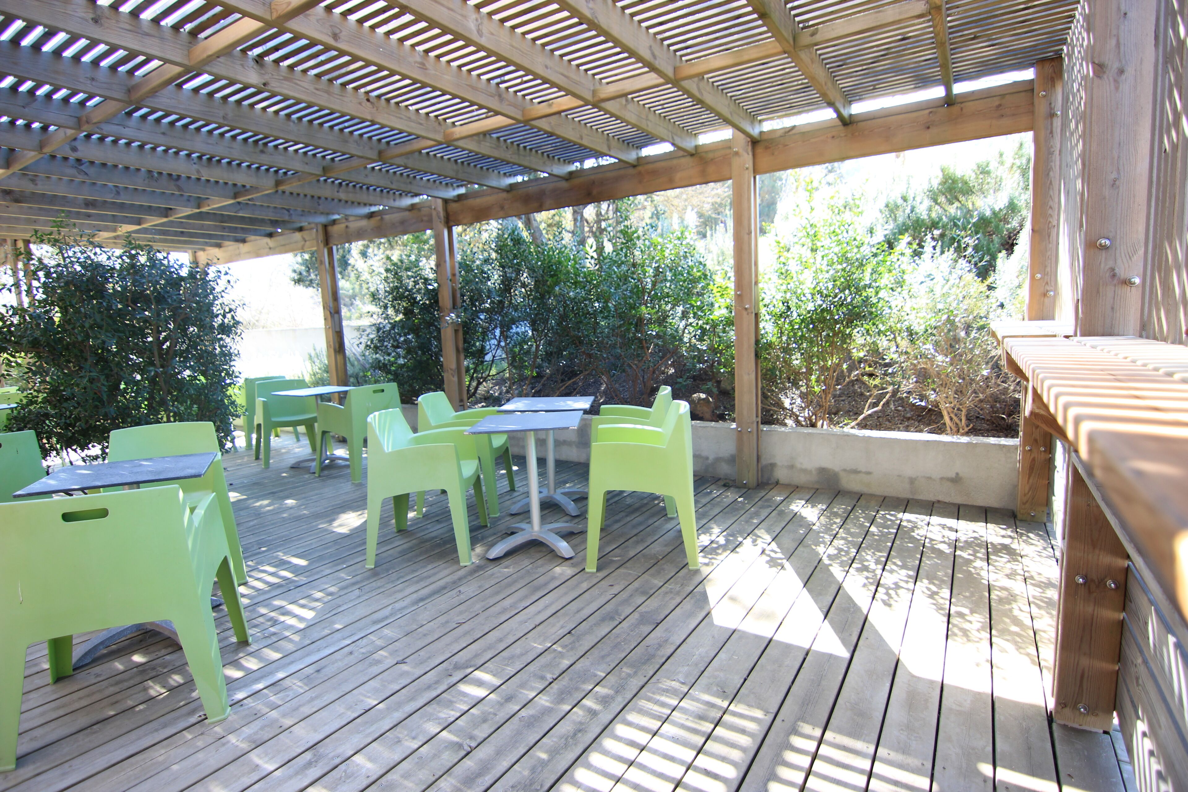 An outdoor patio with wooden flooring, green plastic chairs, and tables.