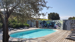 Piscina com deck de madeira, cadeiras de descanso e um muro de pedra com grafites.