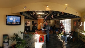 Un hall d’hôtel avec un comptoir d’accueil, un sapin de Noël et un grand écran de télévision diffusant une publicité pour l’hôtel.